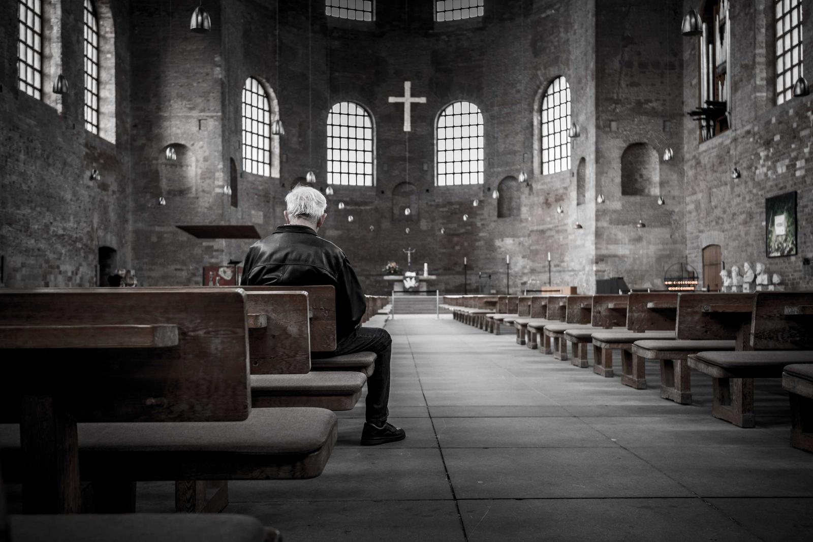 A man sitting in the pews of a stone church with tall arched windows